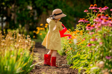 little girl in red rubber boots and a straw hat watering red watering flowers in the garden