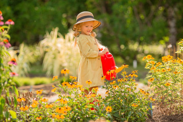 little girl in red rubber boots and a straw hat watering red watering flowers in the garden