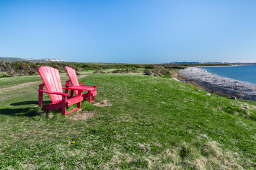 Fototapeta premium Two red adirondack chairs along the coast of Newfoundland, Canada in Gros Morne National Park