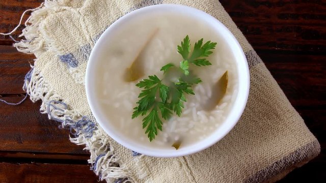 congee in ceramic bowl on rustic wooden table, traditional rice porridge typical of Asian cuisine. Front view