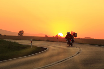 Motocyklista z pasażerem na zakręcie drogi o zachodzie słońca. © Stanisław Błachowicz