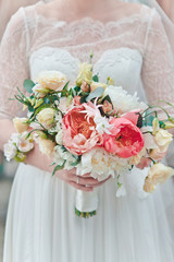 The bride is holding a bouquet of fresh spring and summer flowers in pastel colors on a blurred background, selective focus