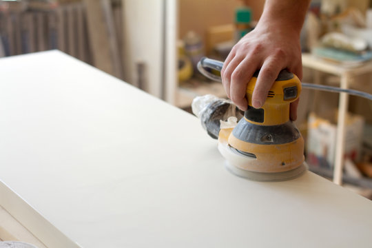 Carpenter grinds the surface of the facade before assembling furniture on a blurred background carpentry workshop, selective focus