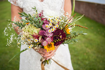 The bride is holding a bouquet of fresh spring and summer flowers in pastel colors on a blurred background, selective focus