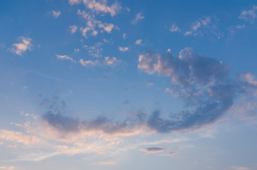 Blauer Himmel mit weißen Wolken in Bogenform mit roter Färbung durch Abendrot bei Sonnenschein am Abend