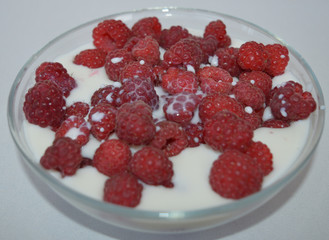 red ripe raspberries in a plate of milk on the table for a delicious snack