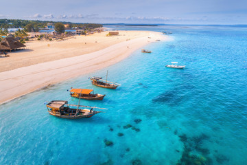 Fototapeta na wymiar Aerial view of the fishing boats on tropical sea coast with sandy beach at sunset. Summer holiday on Indian Ocean, Zanzibar, Africa. Landscape with boat, palm trees, transparent blue water. Top view