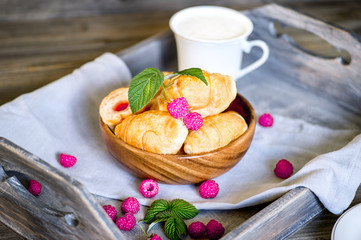 Croissants with raspberries on a wooden tray. The concept of a wholesome breakfast.