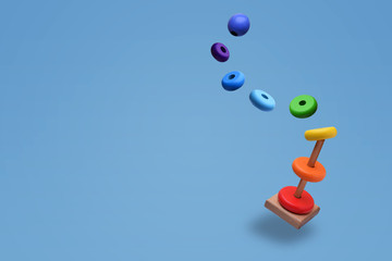 Toy pyramid from rainbow colored wooden rings with a ball head hovers in the air. With flying rings. Toy for babies to joyfully learn mechanical skills and colors. Isolated on light blue background