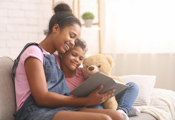 African sisters reading book together at home