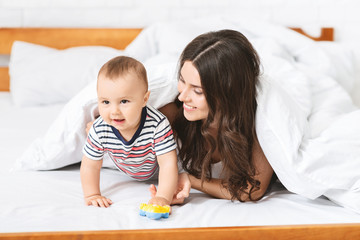 Cheerful young mother playing with adorable baby son in bed
