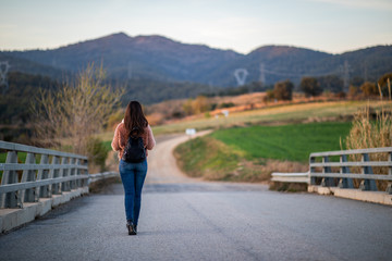 Fototapeta premium Beautiful woman hiking over a bridge with the path and mountains blurred on the background