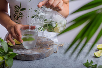 Young woman pouring fresh lemonade from jug into glass