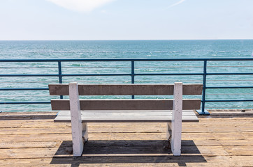 Empty bench on wooden deck, blue sky and sea background