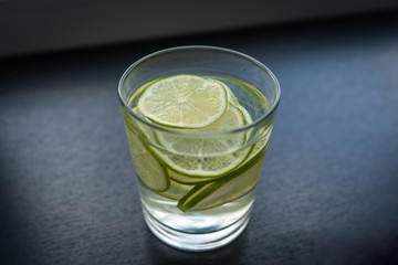 A glass of a refreshing drink, a cocktail with sliced ​​lime on a grey background. Side view