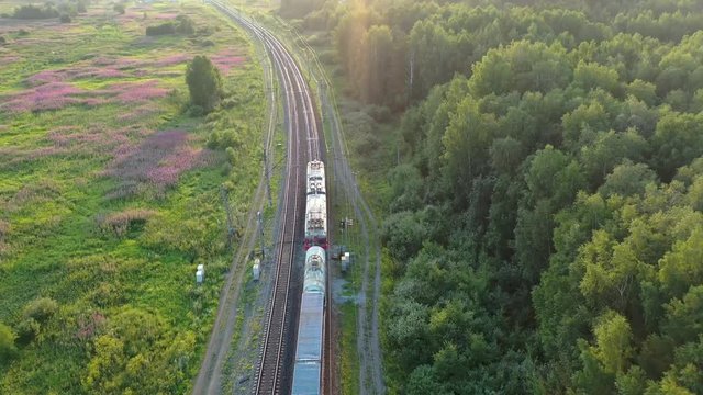 The train goes into the distance in the wild russian forest. Aerial view at sunset. 4k footage from drone