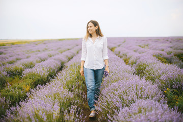 A cheerful young woman is walking in the middle of lavender field.