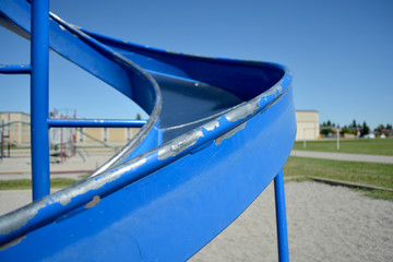 Colourful playground slide in school yard with school in background.