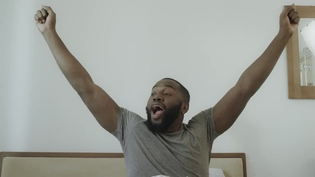 Young guy outstretched arms in bed in morning. Black man dancing in bed.