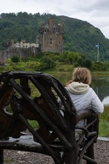 Woman sitting on a wodden park bench looking at a castle in Scotland
