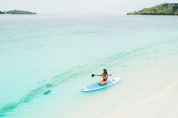 Fototapeta na wymiar Woman paddling on sup board and enjoying turquoise transparent water and white sand island beach. Tropical travel, wanderlust and water activity concept.