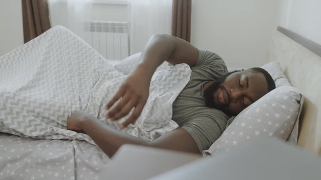 Overslept male person getting up at bedroom. Young guy taking alarm in hands.