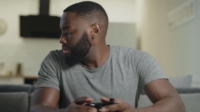 Concentrated man playing game at kitchen. Frustrated guy holding playstation