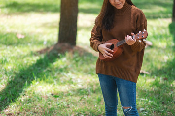 A beautiful asian woman standing and playing ukulele in the park