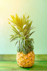 Pineapple on wooden table over neo mint background. Tropical summer vacation and beach party.