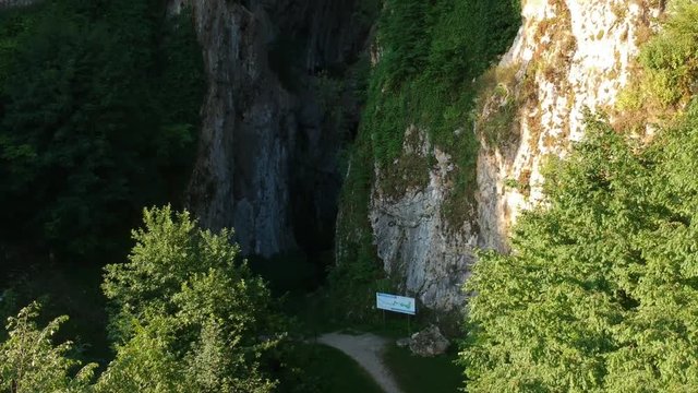 Cliff of Dreznicka Gradina Mountain with the monumental entrance into the Potpec Pecina Cave, drone pedestal up establishing shot