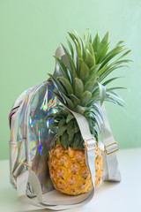 Pineapple with holographic bag on white wooden table over neo mint background. Tropical summer...