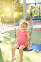 Happy child girl laughing and swinging on a swing at the playground in summer.