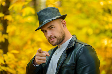 A man on a yellow autumn background. A brutal man with a beard, a black leather jacket and a hat...