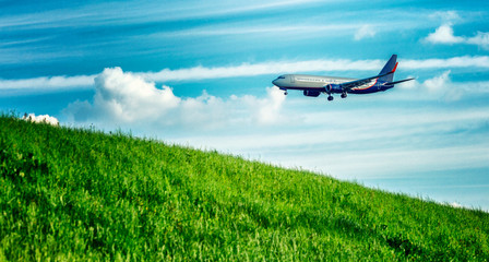 Passenger airplane is landing over a green field. Bright cloudy sky. Panorama.