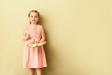 Little girl with brush and palette near color wall