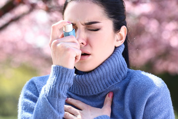 Woman with inhaler having asthma attack on spring day