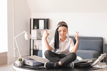 Little businessman meditating while sitting on table in office