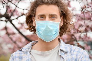 Young man wearing protective mask near blooming tree