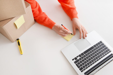Young woman preparing parcel for client at table