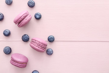 Tasty macarons with blueberry on color wooden background