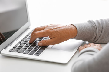 Elderly woman with modern laptop on white table, closeup