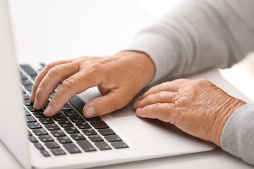 Fototapeta na wymiar Elderly woman with modern laptop on white table, closeup