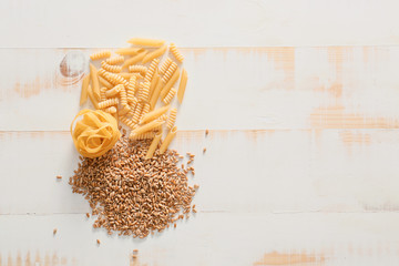 Fototapeta na wymiar Wheat grains with dry pasta on white wooden background