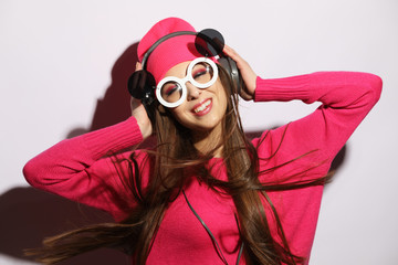 Beautiful young woman wearing pink clothes listening to music in headphones