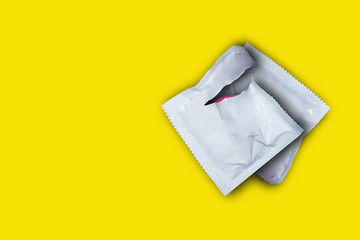 Pink opened condom and condom in pack on a yellow background. Safe sex and reproductive health concept.