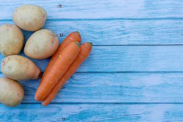 Potatoes and carrots on a blue wooden table background. Cooking ingredients. Harvest. Empty space for text input
