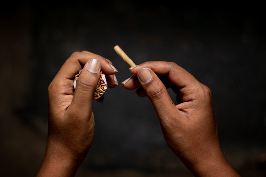 Closeup of Hands holding Beedi or bidi cigarette in dark room.
