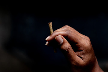 Closeup of Hands holding Beedi or bidi cigarette in dark room.