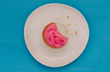 Pink bitten cupcake on a plate isolated on blue background. Delicious cake. Top view.