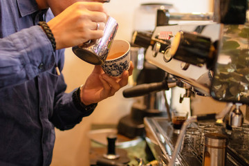 Fototapeta na wymiar Professional barista pouring steamed milk into coffee cup making beautiful coffee. 
